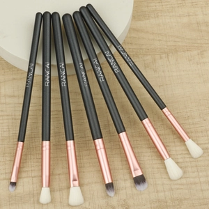 Detailed top view of 7-piece rose gold eye makeup brushes on a wood and white background