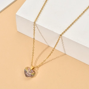 Detail of a gold-plated heart pendant with iridescent zircon on a white stone block