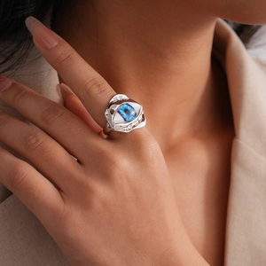 Artistic silver irregular resin ring with blue evil eye detail worn on the finger