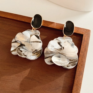 Detailed close-up of marble pattern resin petal earrings with black oval studs on wood