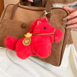 Dettaglio di un ciondolo a forma di pony rosso in peluche su una borsa marrone