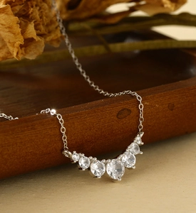 Close-up of curved silver necklace with sparkling zircons on a dark wood background