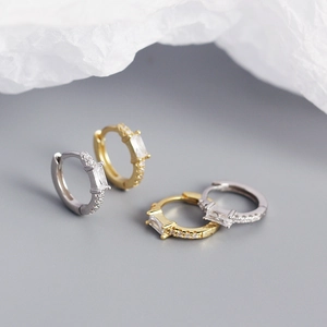 Detailed close-up of gold and silver rectangular zircon hoop earrings on grey surface