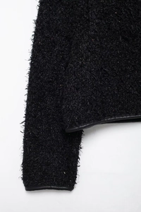 Détail de veste en tweed noir avec texture pelucheuse et liseré en cuir sur la manche