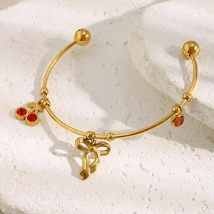 Bracelet jonc doré 18K avec breloques cerise et nœud papillon sur fond de pierre