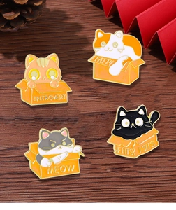 Detailed close-up of four cat-in-box enamel pins with funny slogans on wooden surface