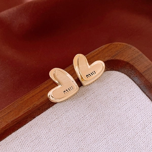 Vue macro de boucles d'oreilles cœur dorées avec gravure miu sur bois sombre