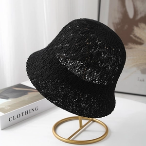 Women's black hollow-out knit bucket hat with breathable texture on a gold metal stand