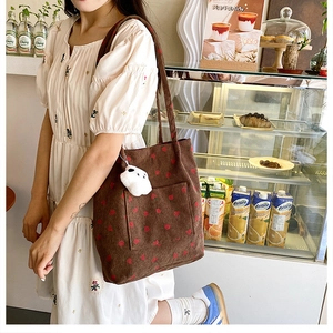 Detail of strawberry pattern corduroy tote bag with plush cloud pendant in cafe setting