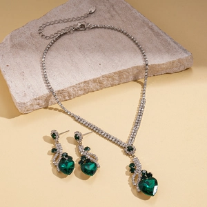 Luxury heart jewelry set with green crystals and silver plating on stone background