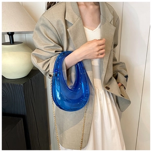 Blue acrylic dinner box bag with gold chain strap held by a model in a stylish indoor setting