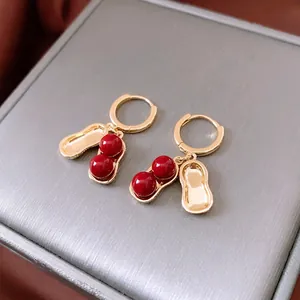 Elegant gold-plated peanut earrings with red beads on a textured jewelry box