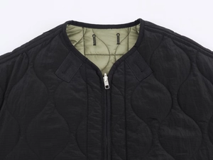 Detail of black quilted jacket with olive green collar lining and silver metal zipper