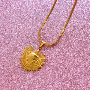 Collier Sacred Heart doré avec texture rayonnante sur fond de paillettes roses