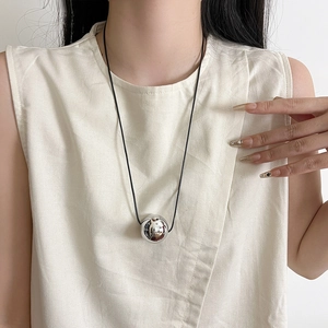 Detail of silver sphere pendant on a thin black cord worn by a model in soft lighting