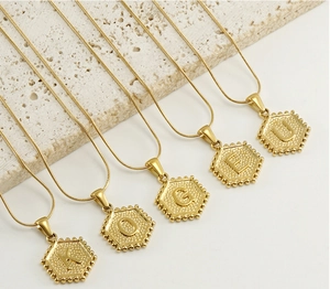 Détail de pendentifs hexagonaux avec lettres en plaqué or 18k et chaînes de type serpent