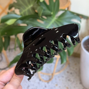 Macro detail of a large black glossy shark hair claw clip held against green leaves