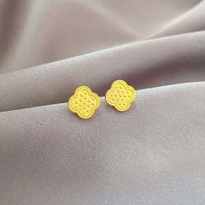 Minimalist golden four-leaf clover stud earrings on grey fabric background