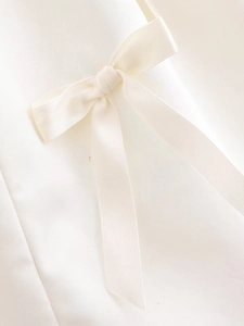 Close-up of a white satin bow detail on a premium elegant women's top fabric
