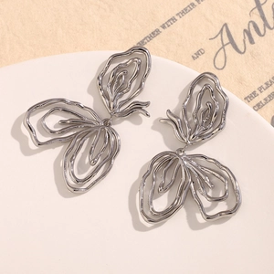 Macro shot of silver abstract butterfly earrings with layered metal design on white tray