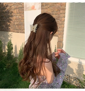 Detailed close-up of matte butterfly hair claw clip worn on wavy hair in sunlight