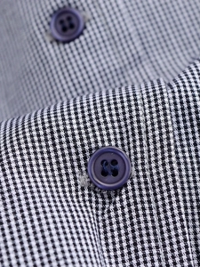 Macro detail of black and white plaid fabric texture with dark blue four-hole button