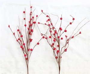 Close-up of vibrant red artificial berry branches on a white plush holiday background