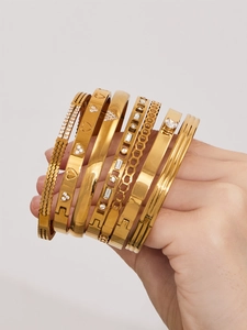 Détail de sept bracelets en acier doré ornés de cristaux et motifs de cœur géométriques