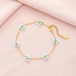 Detail of gold-plated stainless steel bracelet with blue crystal flowers on pink fabric