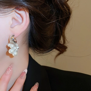 Close-up of elegant C-shaped cluster pearl earrings worn on ear with silver finish