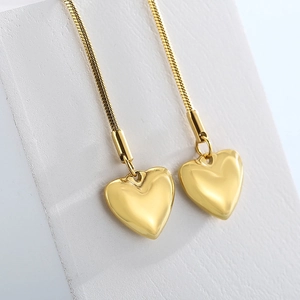 Minimalist gold heart pendant on snake chain draped over a white geometric sculpture