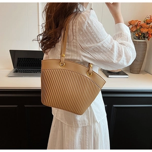 Detail of khaki pleated tote bag with golden metal ring buckle on a white lace top