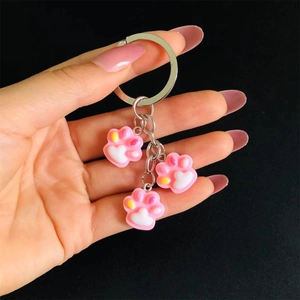 Detail of pink resin cat paw charms on a silver metal keychain held against black background