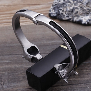 Detail of wolf head stainless steel bangle with black braided leather on dark wood