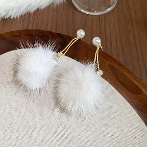 Close-up of gold-plated earrings with white pearls, zircons and fluffy fur balls