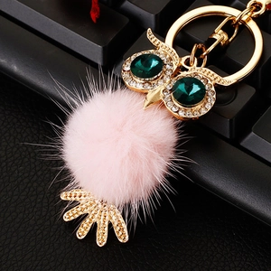 Detail of owl keychain with green rhinestone eyes and soft pink fur pompom on gold ring