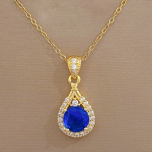 Detail of gold waterdrop pendant featuring a central blue gemstone with pavé crystal accents