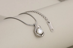 Macro shot of stainless steel snake chain necklace with pearl pendant and logo tag