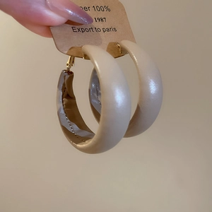 Detail of light beige leather hoop earrings with fine stitching and gold-toned metal clasp
