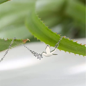 Close-up of S925 sterling silver bird necklace with sparkling zircons on green leaf