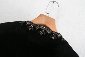Détail de la broderie à paillettes dorées sur haut en velours de soie noir avec vue du col