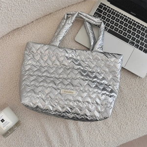 Detail of silver heart-quilted tote bag next to a laptop and candle on beige fabric