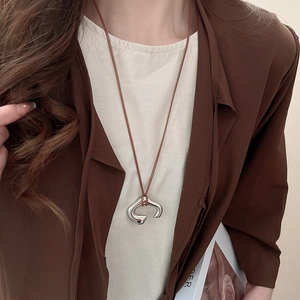 Detail of silver irregular C-shaped pendant on long brown cord necklace worn by model