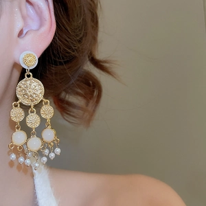 Gros plan d'une boucle d'oreille à pampille dorée avec perles et détails en relief sur modèle