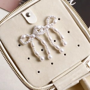 Detailed close-up of a handmade pearl bow brooch displayed in a cream velvet jewelry box