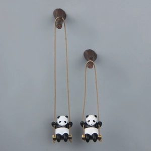 Detailed view of 3D panda swinging on branch ornaments against a grey wall background