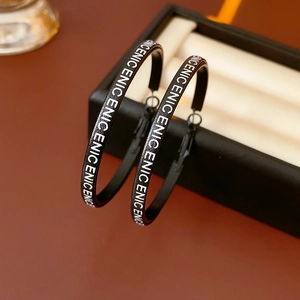 Gros plan de créoles en cuir noir avec lettres ENIC blanches sur un écrin à bijoux