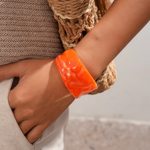 Close-up of vibrant orange wavy acrylic bangle worn on wrist with summer vacation vibes