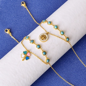Two-layer gold anklet with turquoise beads, tree of life and clover charms on white stand