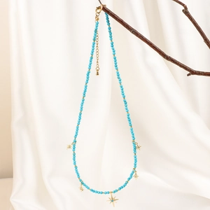 Detail of bohemian sky blue beaded necklace with golden star charms on a branch